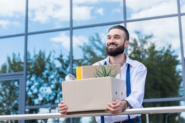 businessman with cardboard box with office supplies in hands standing outside office building, quitting job concept